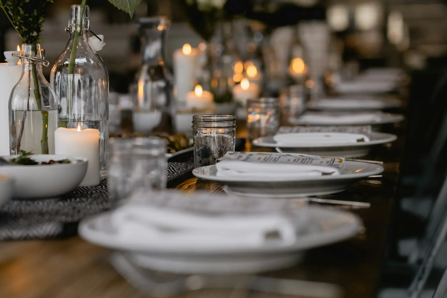 Long dinner table set with white plates and glowing candles