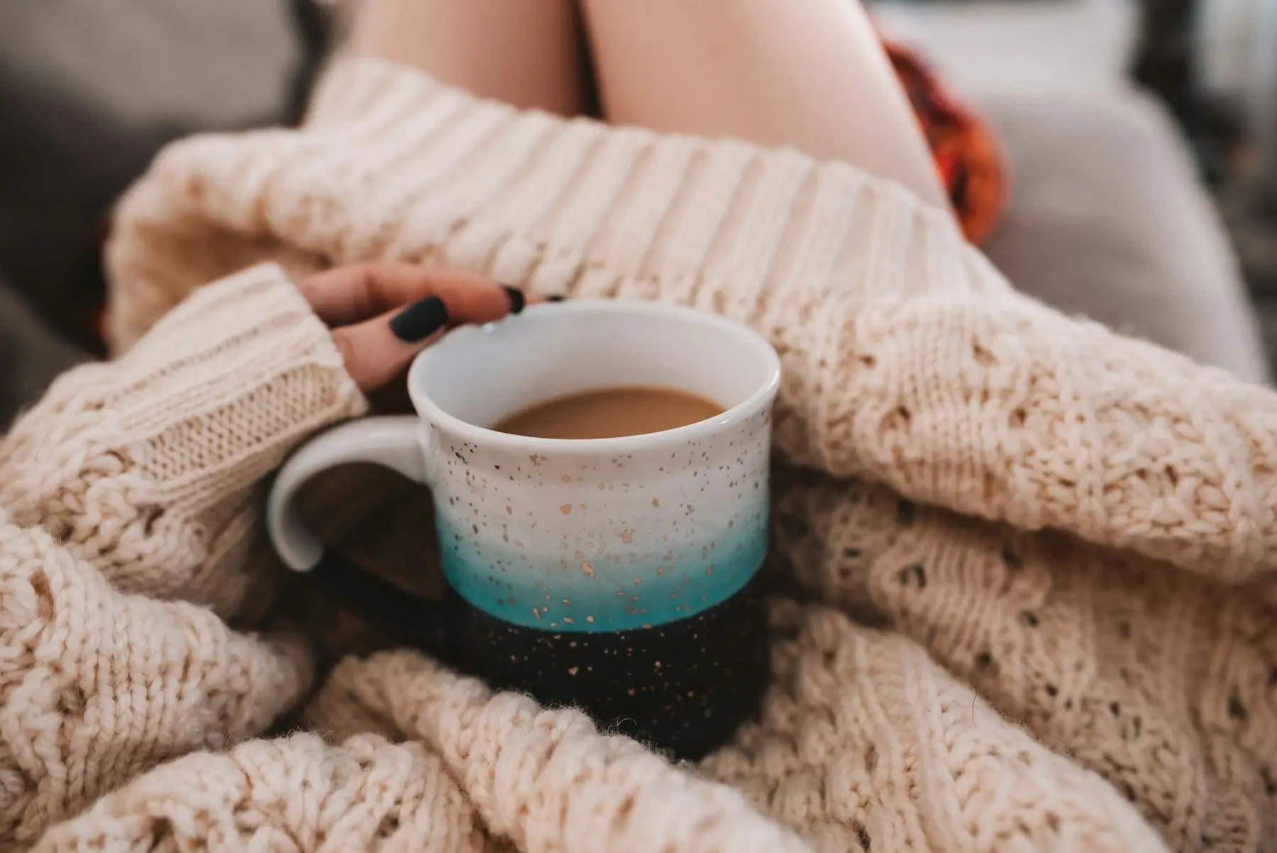 Mains tenant une tasse de café, enveloppées dans un chandail en tricot crème